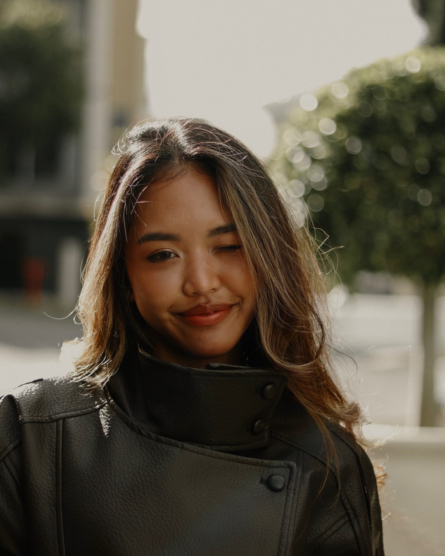 Kara Chaliaowai smiling in a black leather jacket, backlit in afternoon sun